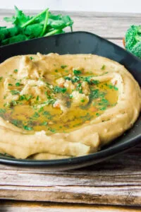 Ingredients for tahini-free hummus: garbanzo beans, olive oil, lemon, garlic powder, and salt arranged on a wooden surface.