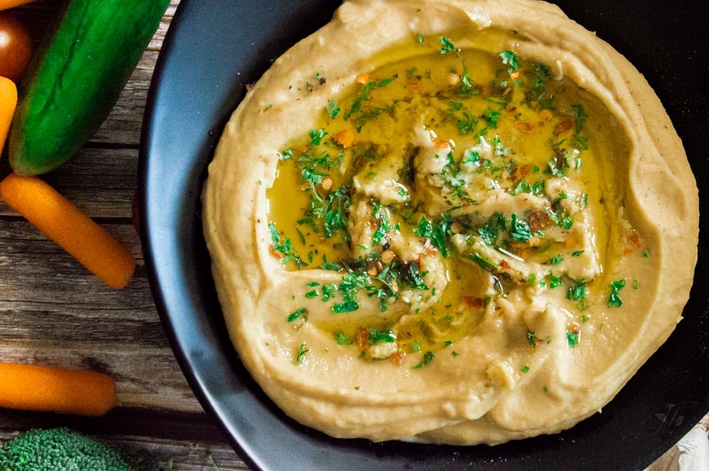 Close-up of homemade hummus spread on a slice of whole-grain bread topped with fresh herbs.