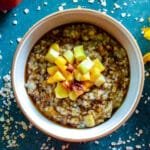 A bowl of creamy Maple Brown Sugar Fruity Oats topped with fresh apple and peach slices, a drizzle of maple syrup, and a sprinkle of pumpkin spice.
