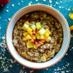 A bowl of creamy Maple Brown Sugar Fruity Oats topped with fresh apple and peach slices, a drizzle of maple syrup, and a sprinkle of pumpkin spice.
