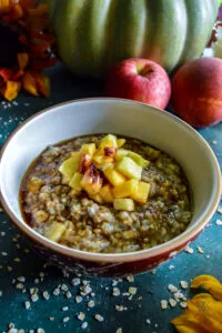 A cozy breakfast scene with a steaming bowl of Maple Brown Sugar Fruity Oats, a wooden spoon, and fall-themed decor in the background.