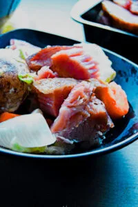 Close-up of ham shank simmering in a large pot surrounded by fresh vegetables.