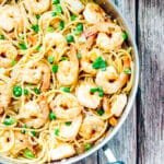 Finished dish of shrimp pasta with a side of lemon slices and a glass of white wine for a complete meal look.
