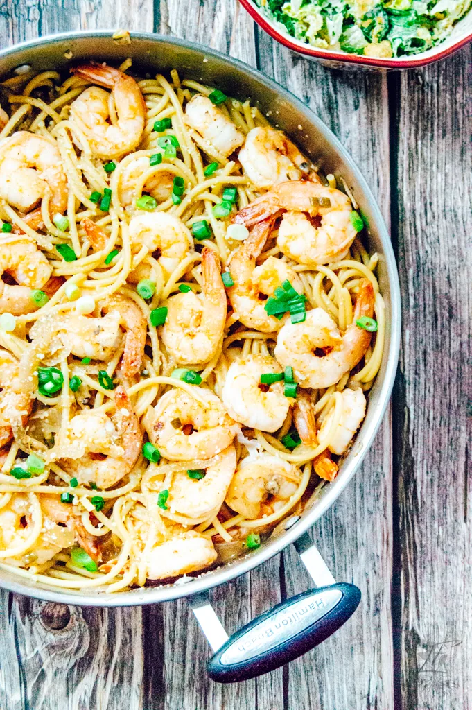 Finished dish of shrimp pasta with a side of lemon slices and a glass of white wine for a complete meal look.
