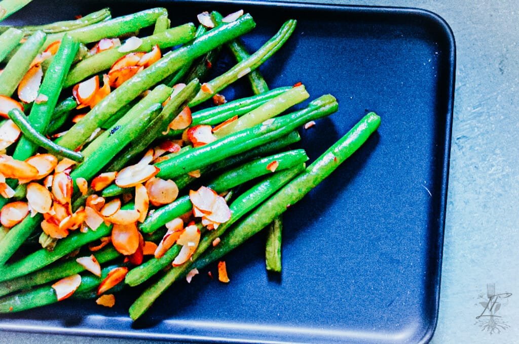 A close-up of sautéed green beans with sliced almonds in a cast-iron skillet, glistening with melted butter.