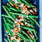 A plated serving of Almond Green Beans garnished with a sprinkle of kosher salt, placed on a rustic dining table.