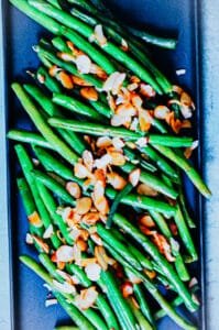 A plated serving of Almond Green Beans garnished with a sprinkle of kosher salt, placed on a rustic dining table.
