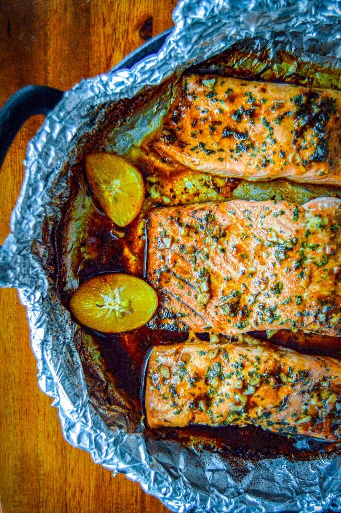 A close-up of flaky, golden-baked Spicy Garlic Salmon topped with fresh cilantro and served with lemon wedges.