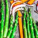 A pan of honey-glazed carrots and asparagus, garnished with fresh herbs, served on a rustic wooden table.