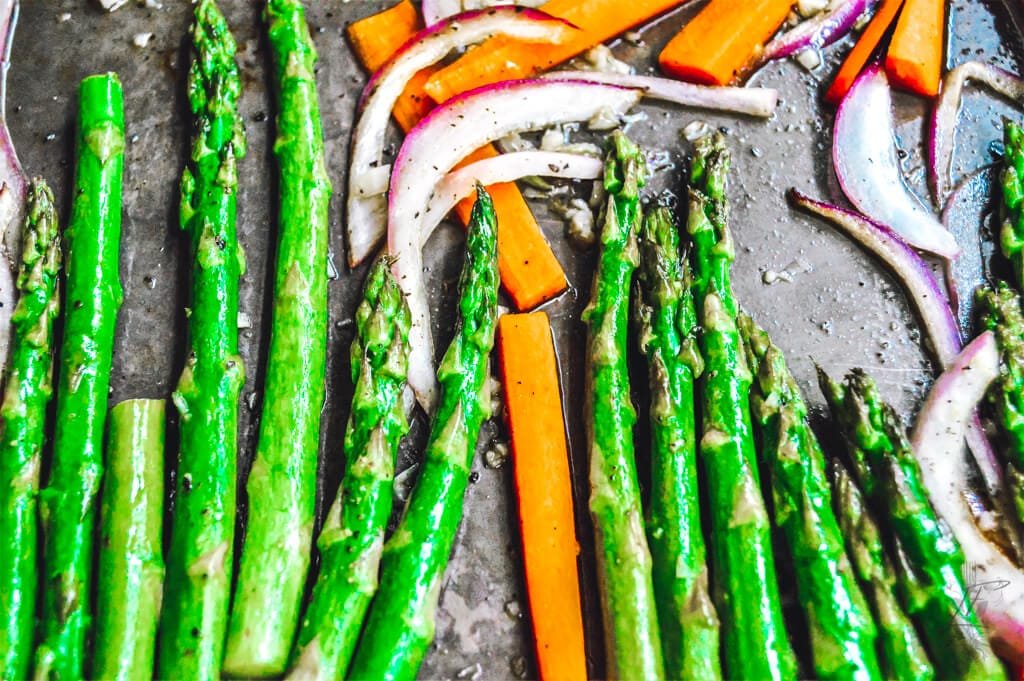 A pan of honey-glazed carrots and asparagus, garnished with fresh herbs, served on a rustic wooden table.