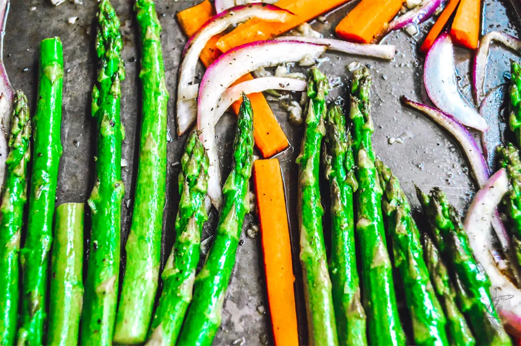 A pan of honey-glazed carrots and asparagus, garnished with fresh herbs, served on a rustic wooden table.