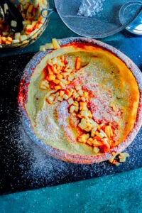 Close-up of Vanilla Almond Dutch Baby Pancake with apples and peaches, and powdered sugar.