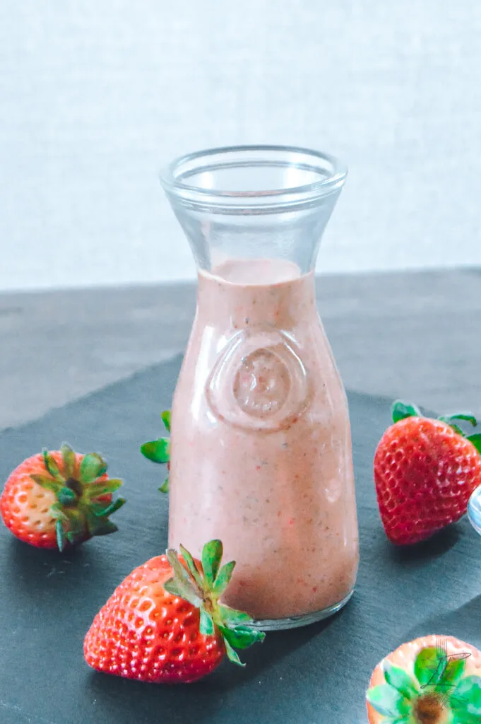 Strawberry balsamic dressing in a jar with fresh strawberries and mint leaves.