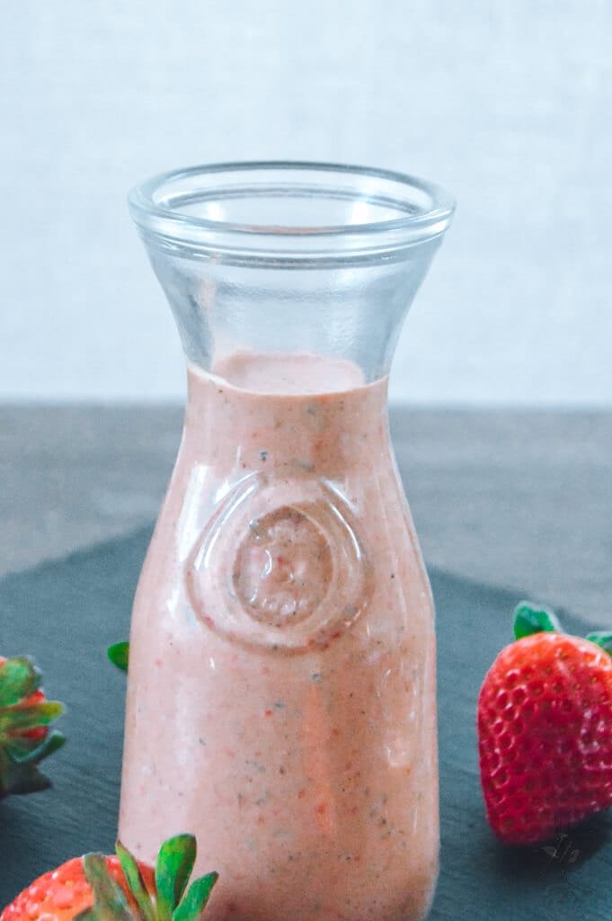 Jar of strawberry balsamic dressing with a fresh salad and sliced strawberries.