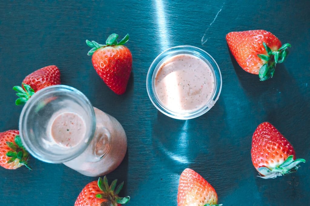 Jar of strawberry balsamic dressing with a fresh salad and sliced strawberries.