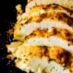 Overhead view of golden roasted cauliflower slices fanned out in a skillet, showing the rich buttery parmesan topping.