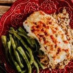 Baked lemon herb halibut served with green beans and wild rice on a red patterned plate.