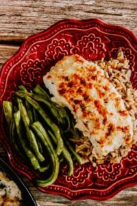 Baked lemon herb halibut served with green beans and wild rice on a red patterned plate.