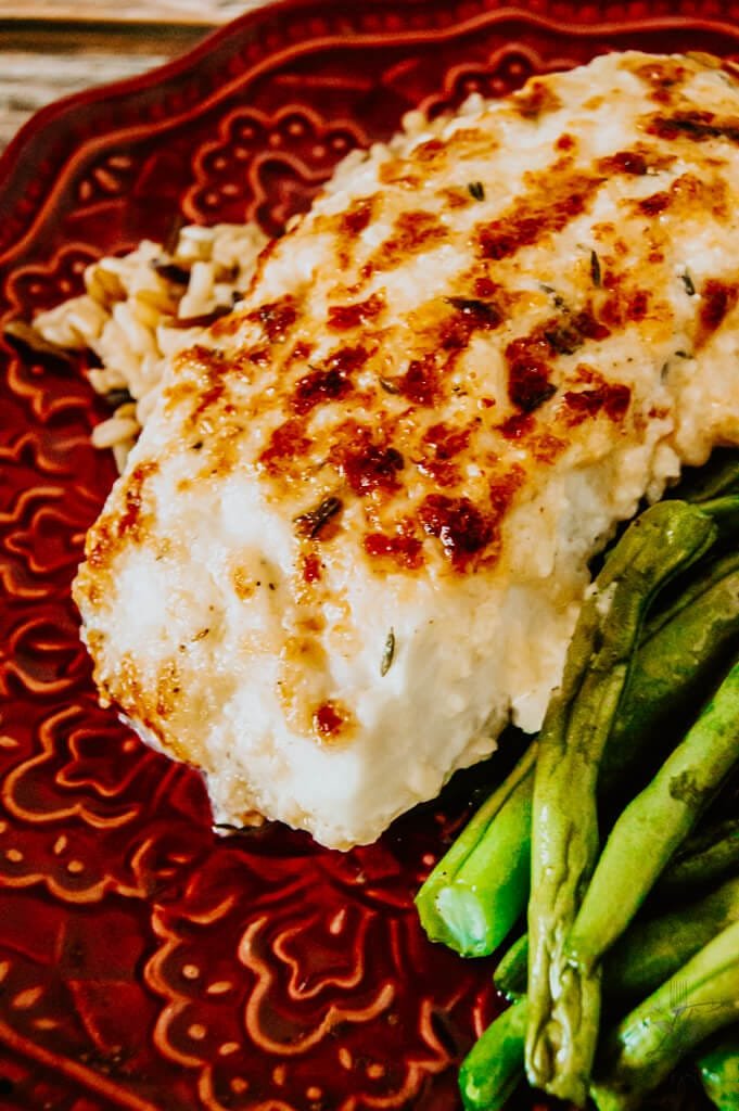 Close-up of golden baked halibut fillet with Parmesan topping, served with green beans and rice.
