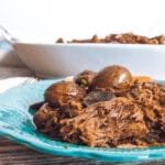 Close-up of shredded chili coffee roast beef and whole baby potatoes on a turquoise plate.