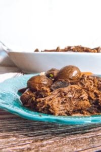 Close-up of shredded chili coffee roast beef and whole baby potatoes on a turquoise plate.