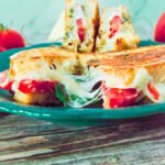 Grilled Caprese sandwich sliced in half on a teal plate, revealing melted cheese, tomato, and basil inside.