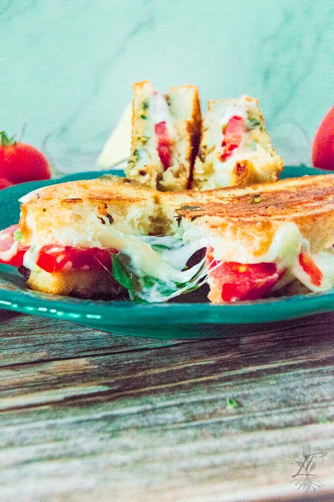 Grilled Caprese sandwich sliced in half on a teal plate, revealing melted cheese, tomato, and basil inside.