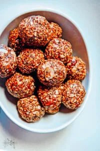 Bowl of glossy chocolate raspberry energy bites made with oats, chia seeds, jam, and hazelnut spread.