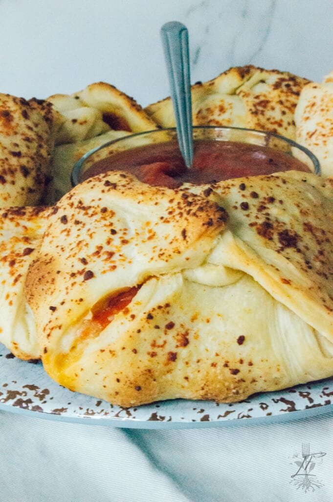 Close-up of a cheesy baked pizza pocket with golden seasoning, served with a side of pizza sauce.