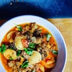 Overhead view of sausage and pepper ravioli served in a white bowl, garnished with fresh basil and grated cheese.