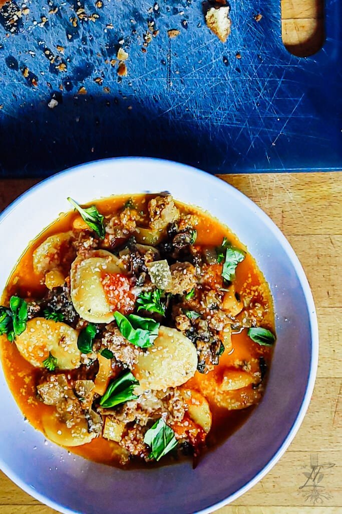 Overhead view of sausage and pepper ravioli served in a white bowl, garnished with fresh basil and grated cheese.