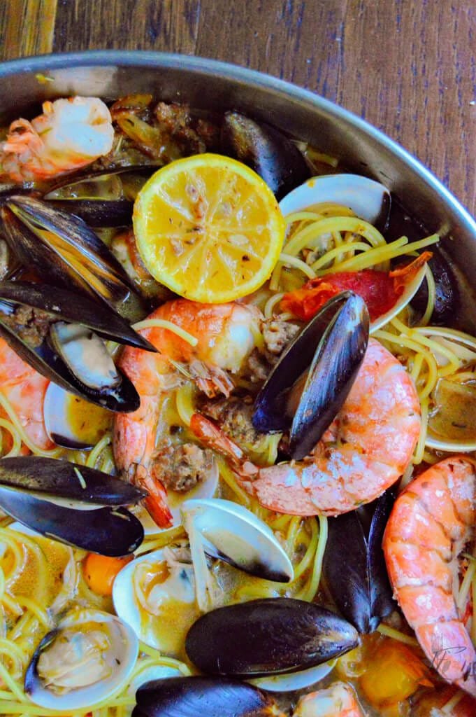 Close-up of seafood pasta featuring mussels, shrimp, clams, and grilled lemon slices on spaghetti in a flavorful broth.