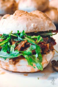 Italian beef sandwich on a plate, loaded with shredded beef, fresh arugula, and served on a fluffy roll.