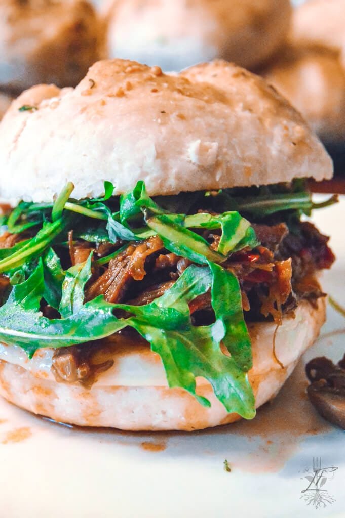 Italian beef sandwich on a plate, loaded with shredded beef, fresh arugula, and served on a fluffy roll.
