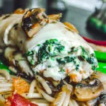 Close-up of spinach and ricotta stuffed flounder fillet topped with sautéed mushrooms, served over spaghetti with bacon and mushroom medley.