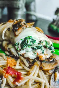 Close-up of spinach and ricotta stuffed flounder fillet topped with sautéed mushrooms, served over spaghetti with bacon and mushroom medley.